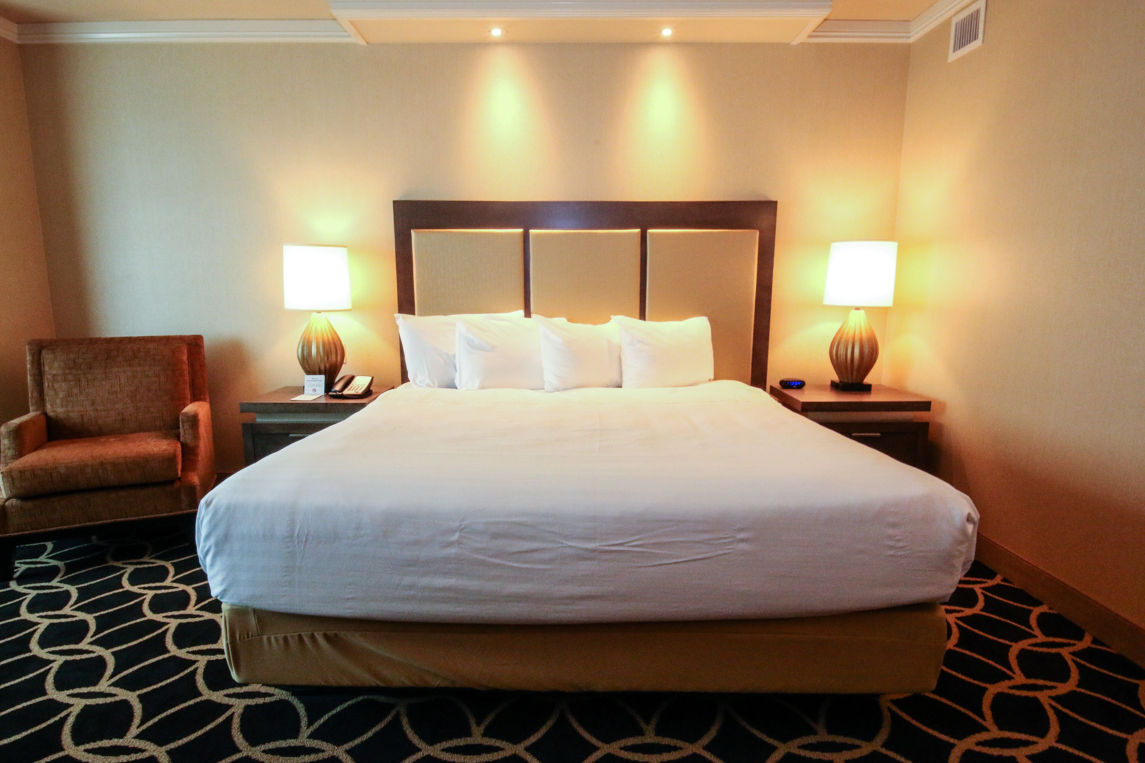 Habitación de hotel con una cama grande, dos mesitas de noche con lámparas, una silla y una alfombra estampada.