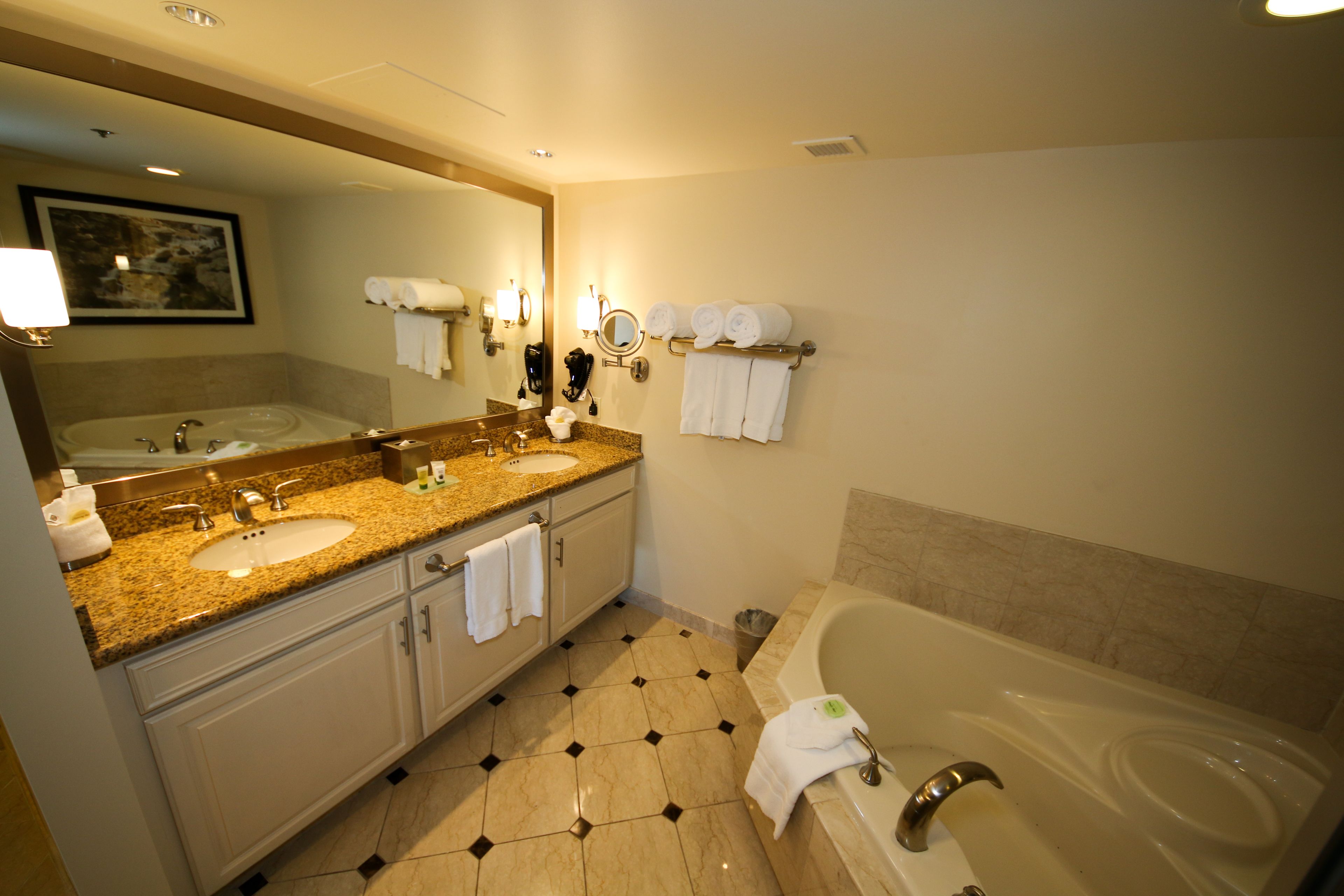 A hotel bathroom with two sinks, a large mirror, a bathtub, and a towel rack with towels.