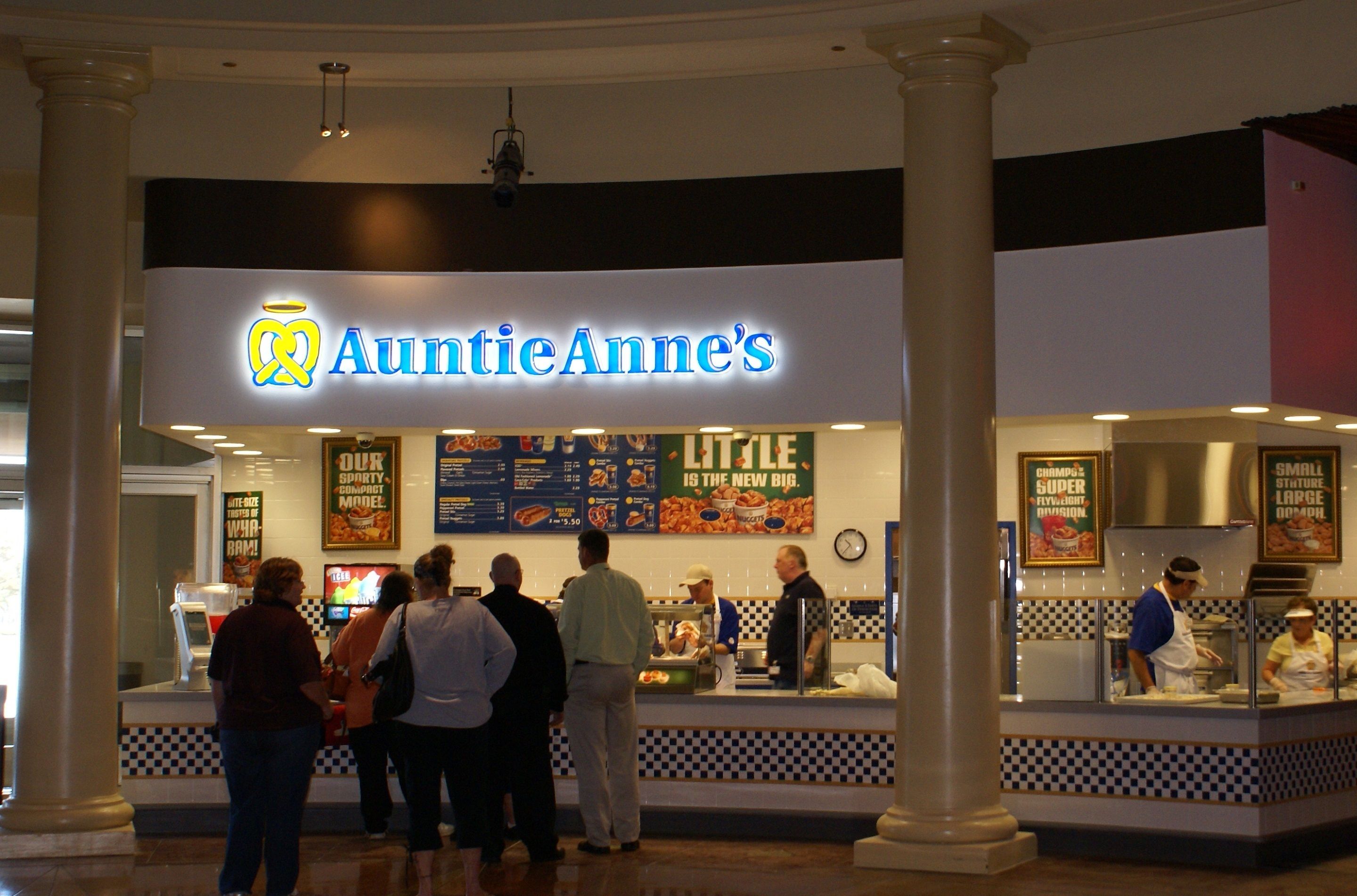 Zona de comidas con un letrero destacado de 'AuntieAnne's', que muestra un logotipo y la carta.