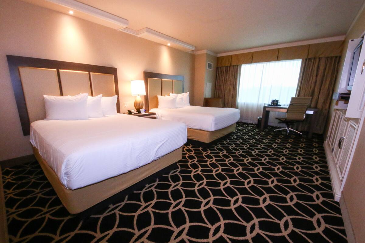 Una habitación de hotel con dos camas, un escritorio, una silla y un ventanal con cortinas.