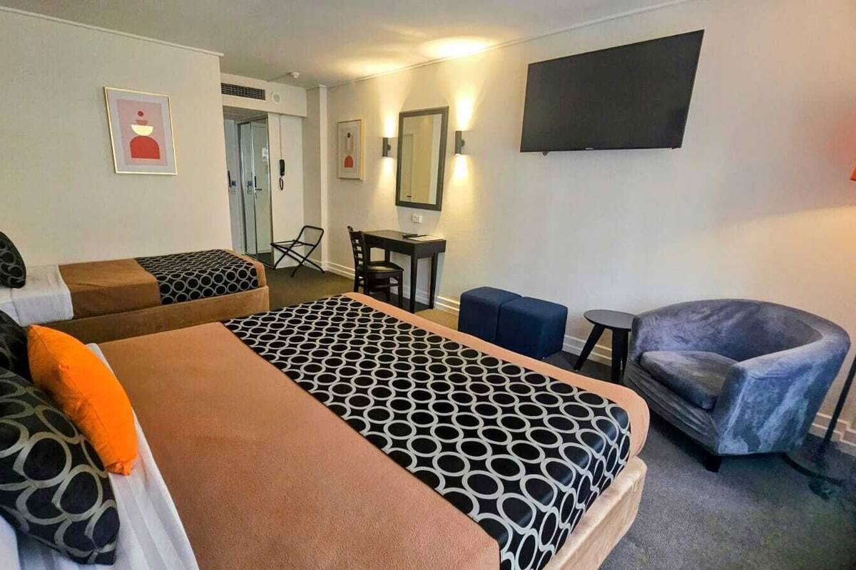 A hotel room with two beds, a desk, a chair, and a TV.