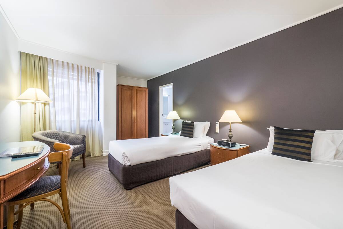 Ein Hotelzimmer mit zwei Betten, einem Schreibtisch mit Stuhl und zwei Nachttischen mit Lampen.