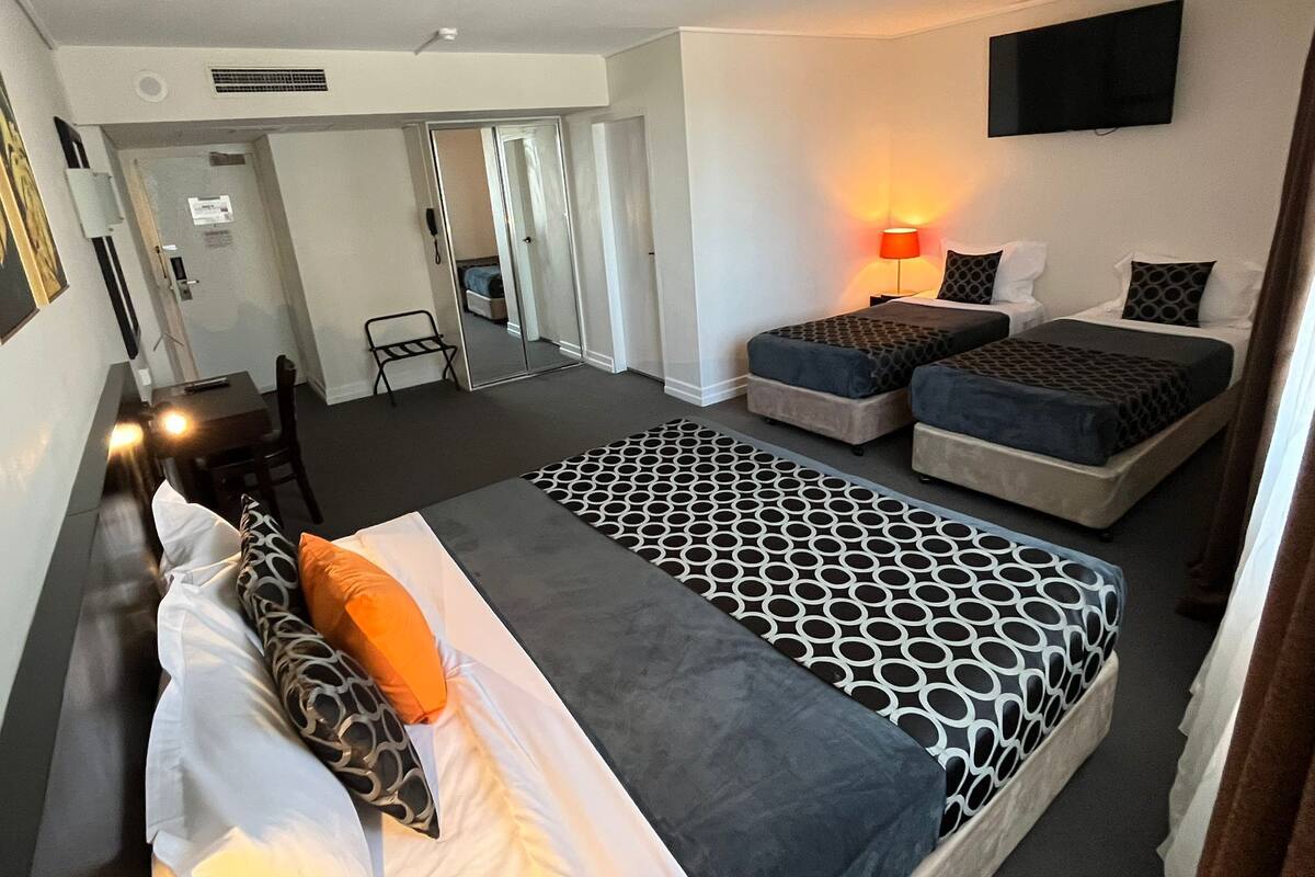 A hotel room with a large bed, two bedside tables, a TV mounted on the wall, and a desk with a chair.