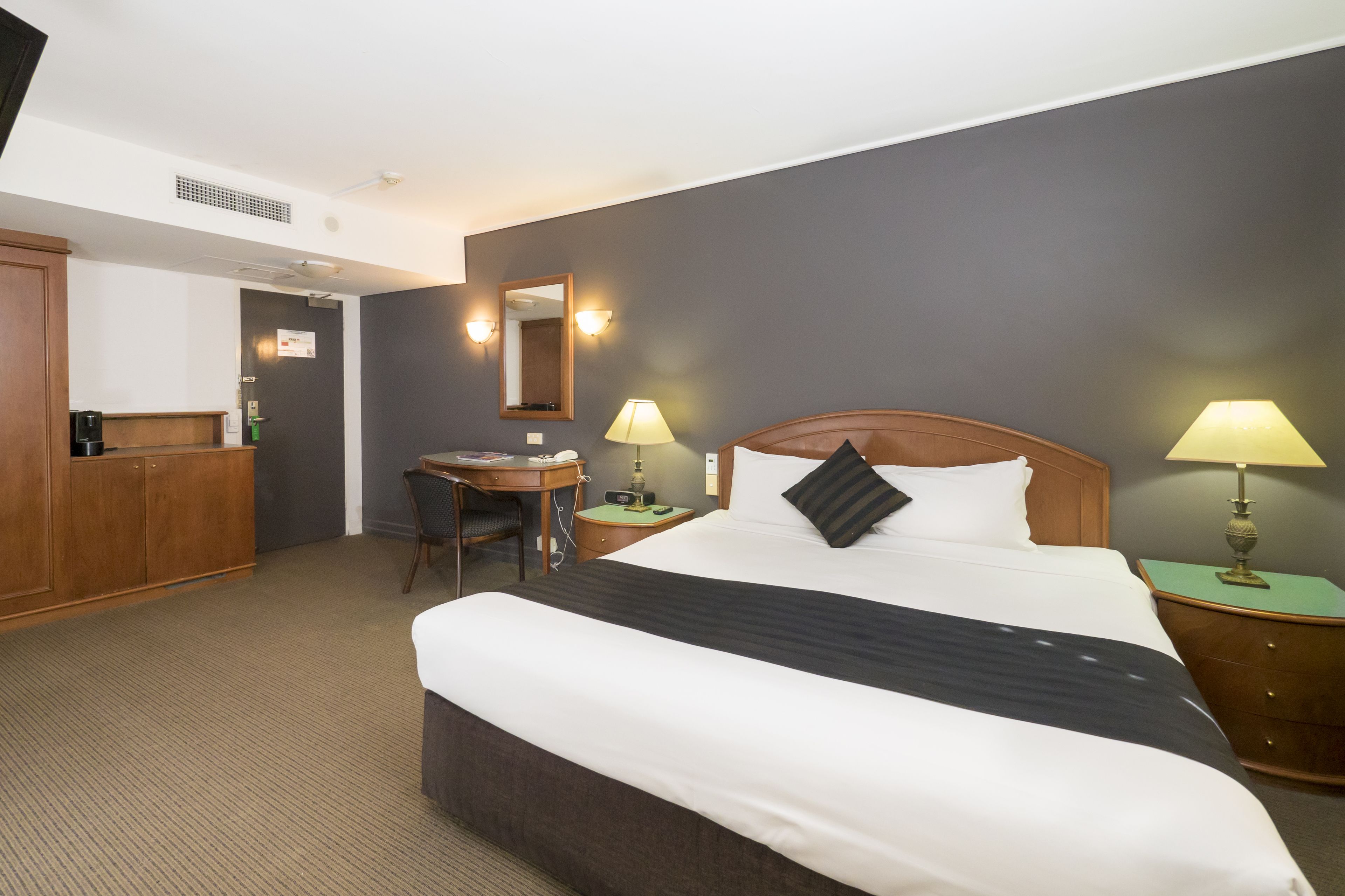 A hotel room with a large bed, a desk, a chair, and two bedside tables with lamps.