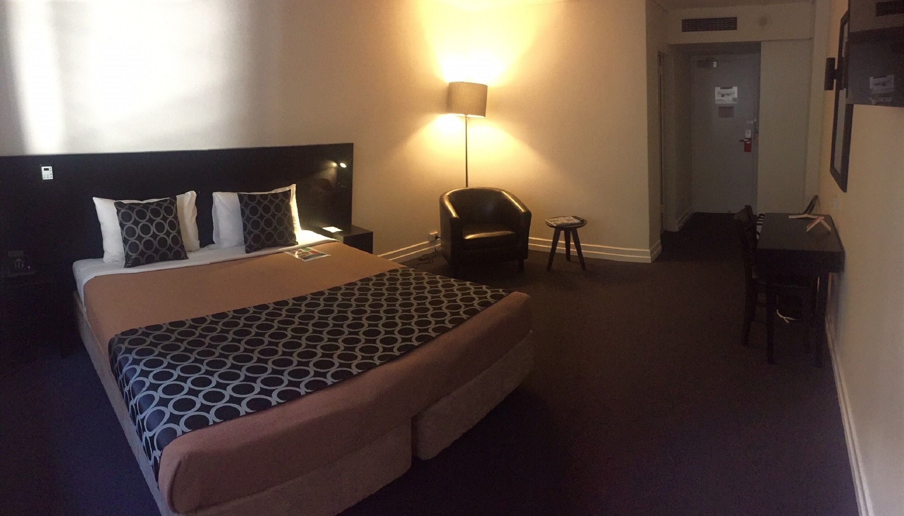 Habitación de hotel con una cama grande, un escritorio, una silla y una lámpara.