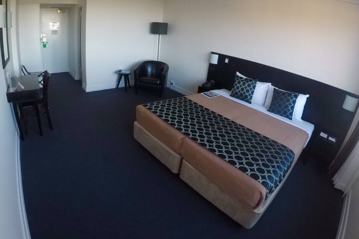 A hotel room with a bed, a desk, a chair, and a lamp.