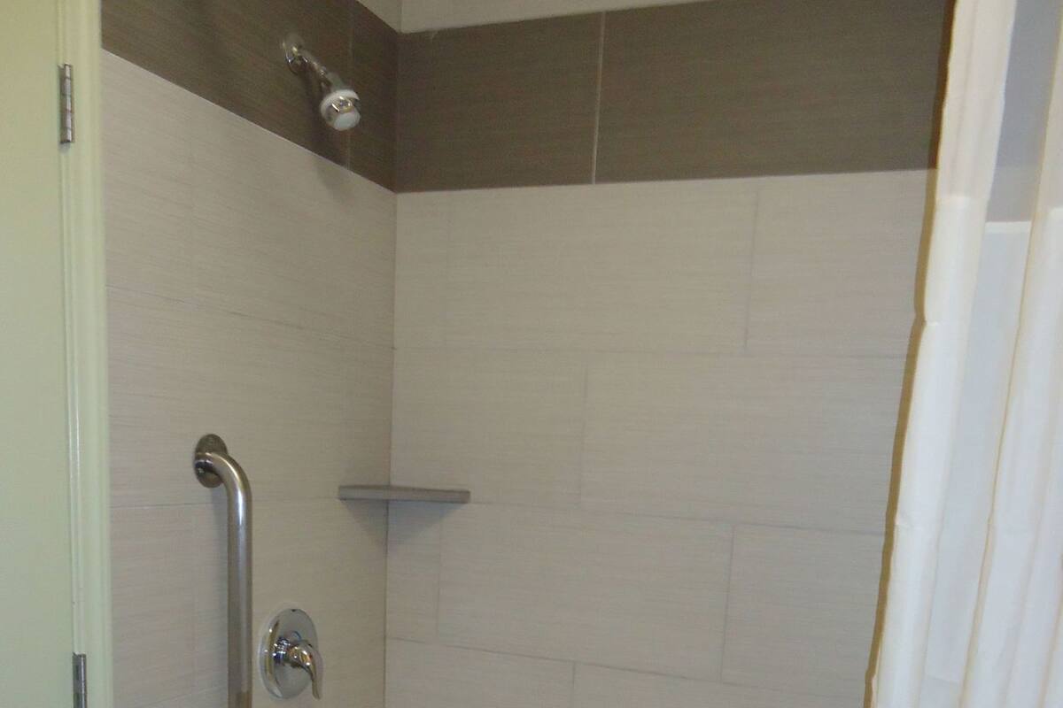 A bathroom with a bathtub, a shower curtain, and a handrail.