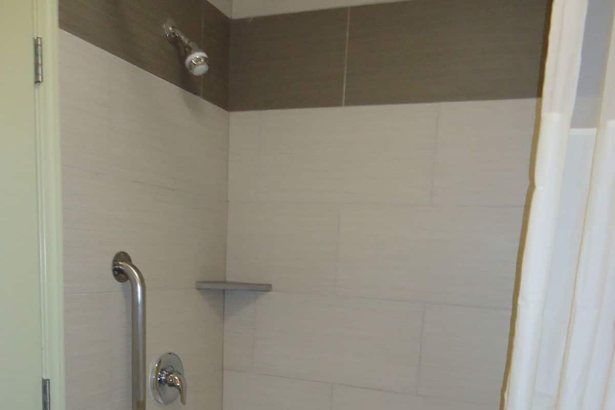 A bathroom with a bathtub, a shower curtain, and a handrail.