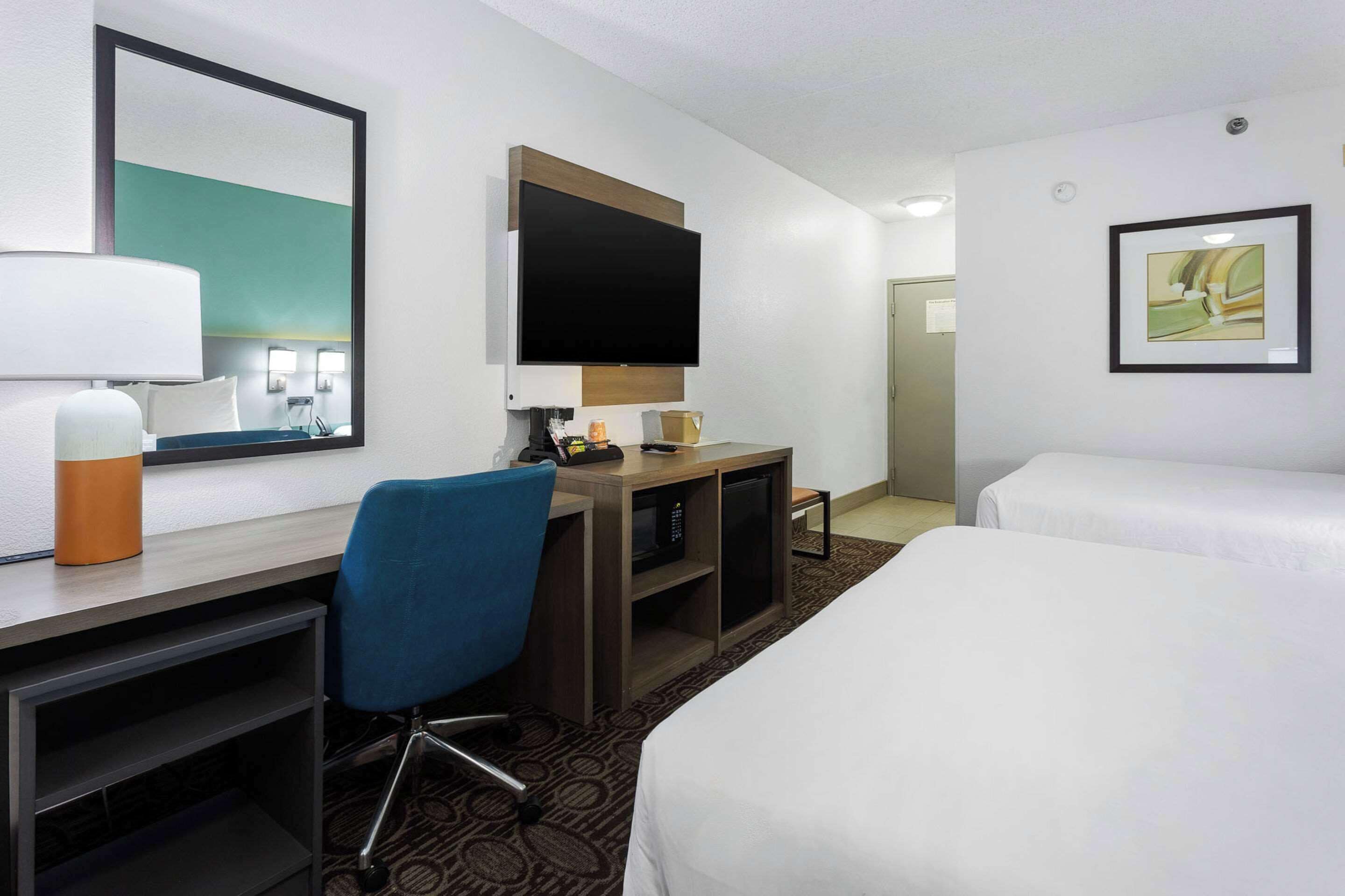 A hotel room with a bed, a desk with a chair, a television, and a framed picture on the wall.