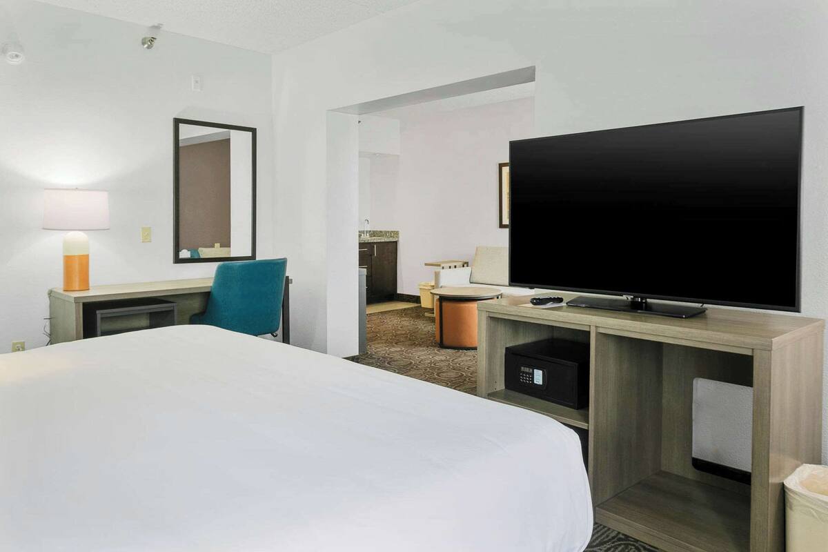 A hotel room with a large bed, a desk with a lamp, a television, and a mirror.