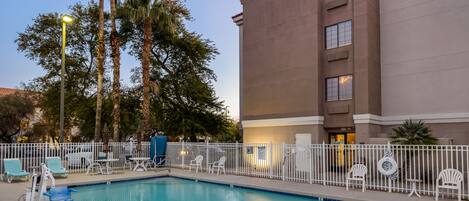 Un hotel Comfort Inn con piscina, rodeado de palmeras y un patio cercado con sillas de descanso.