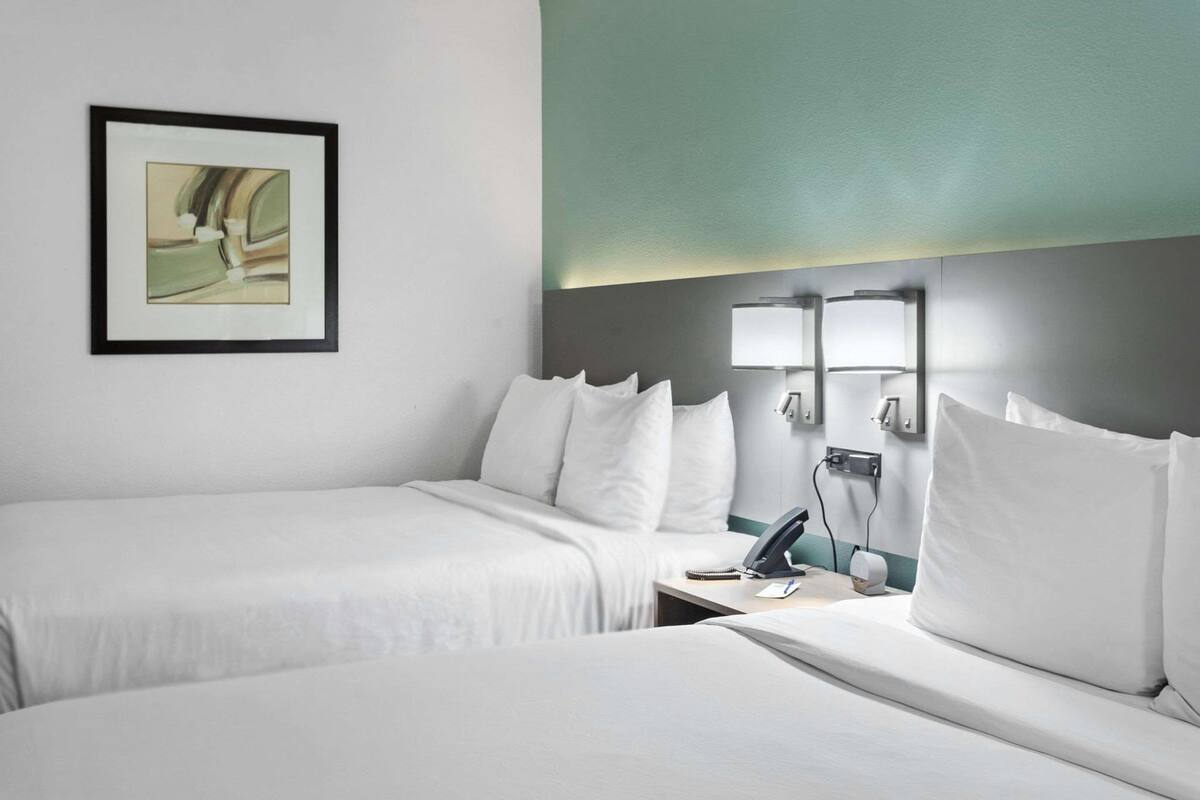 A hotel room with two beds, a framed artwork on the wall, and a bedside table with a lamp.