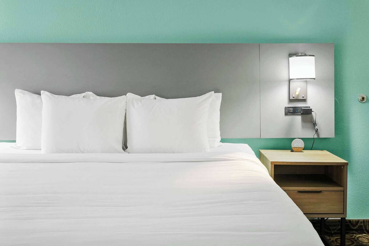 A hotel room with a large bed, a nightstand with a lamp, and a wall-mounted light fixture.