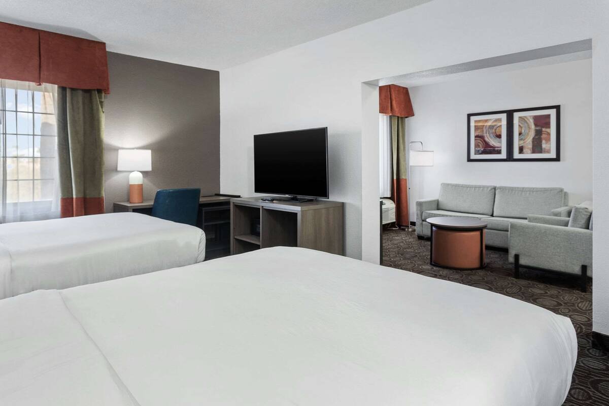 A hotel room with two beds, a desk with a television, a sofa, a coffee table, and artwork on the wall.