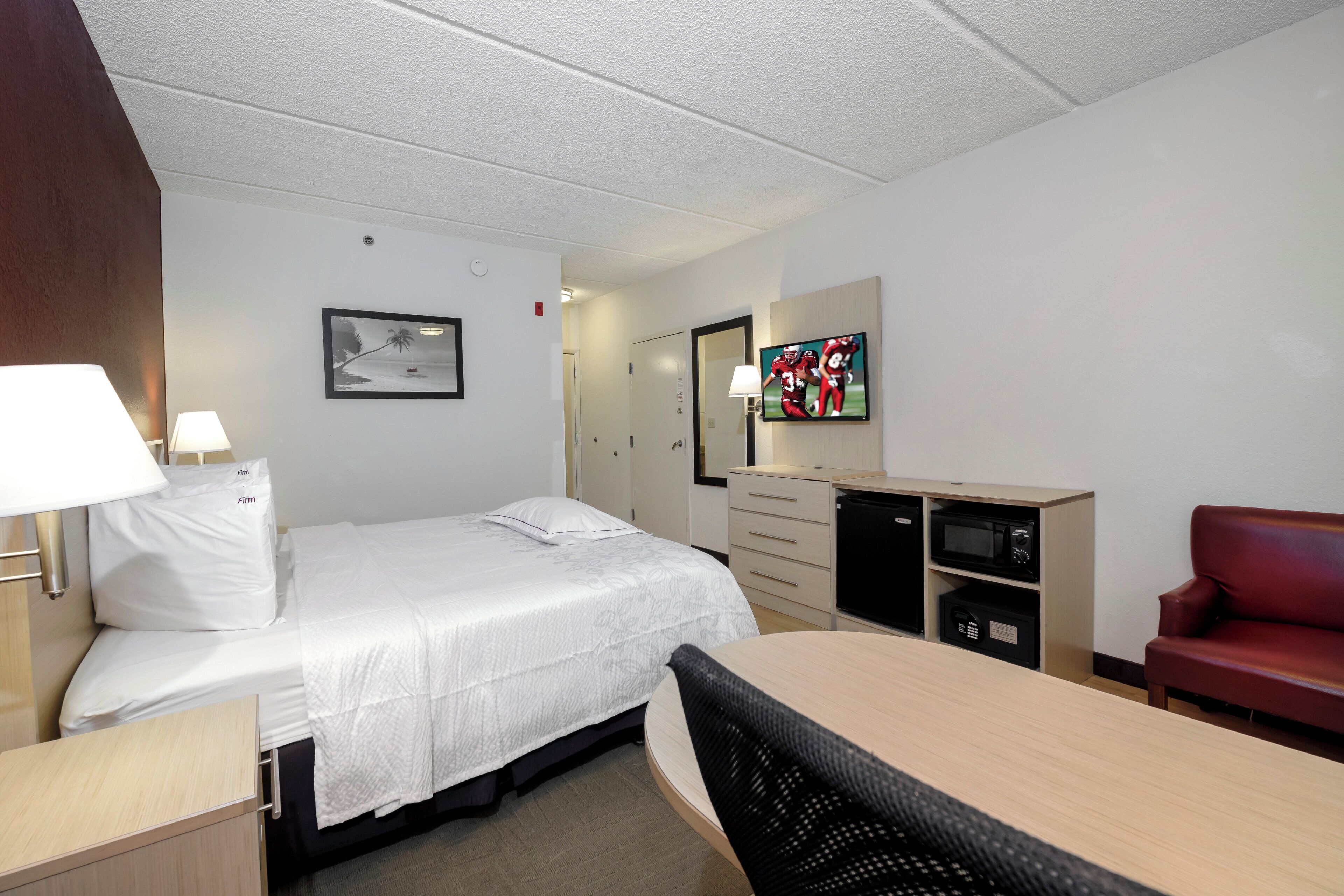 Een hotelkamer met een bed, een bureau, een stoel, een televisie en een magnetron.