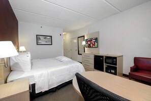 Hotellihuone, jossa on sänky, työpöytä, tuoli, televisio ja mikroaaltouuni.