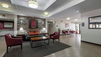 Un vestíbulo de hotel con pared de piedra, un letrero de 'Red Roof Plus', sillones de cuero, una mesa de centro de madera y un mostrador de recepción.