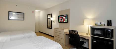 Habitación de hotel con dos camas, un escritorio, una silla, un televisor, un microondas y una cafetera.