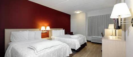 A hotel room with two beds, a desk, and a lamp.