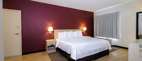 A hotel room with a bed, bedside lamps, a window with curtains, and a wooden floor.