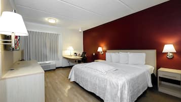 Habitación de hotel con cama, mesitas de noche, escritorio, silla, lámpara, cortina y aplique de pared.