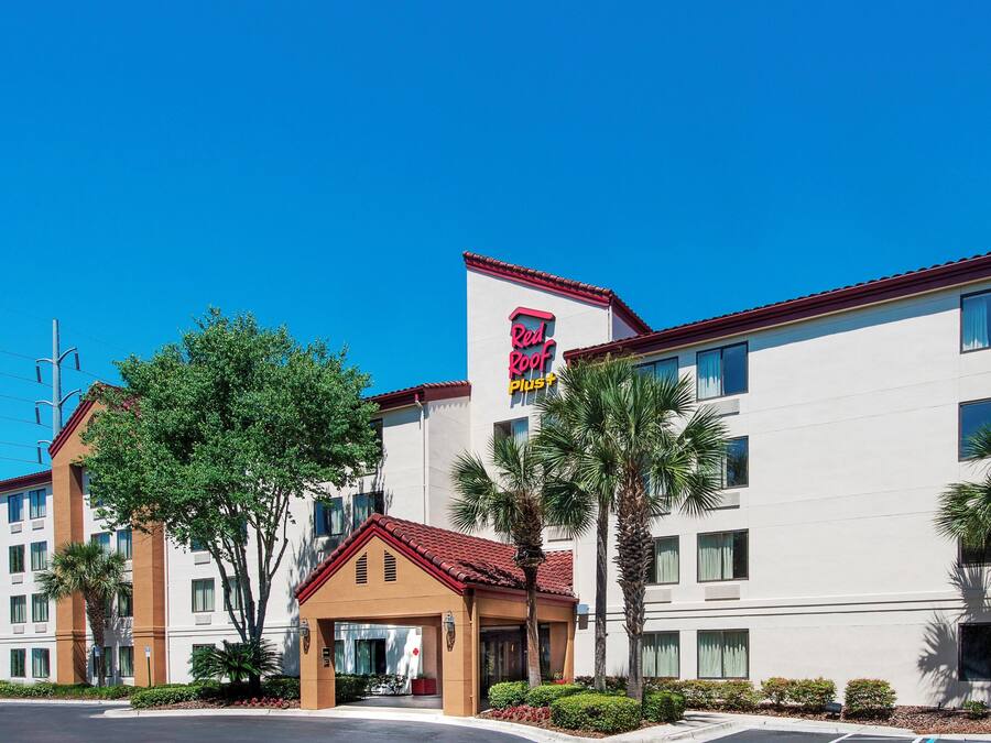 Un hotel con techo rojo, un letrero de 'Red Roof Plus' y un edificio con múltiples ventanas y balcones.