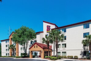 A hotel with a red roof, a 'Red Roof Plus' sign, and a building with multiple windows and balconies.