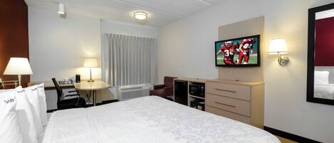 A hotel room with a bed, a desk, a television, and a minibar.