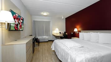 A hotel room with a bed, desk, chair, lamp, and a television on the wall.