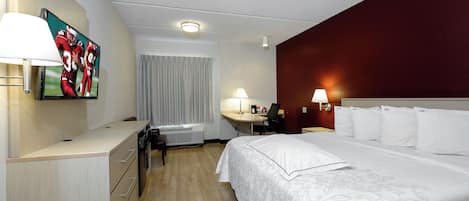 Une chambre d’hôtel équipée d’un lit, d’un bureau, d’une chaise, d’une lampe et d’un téléviseur fixé au mur.