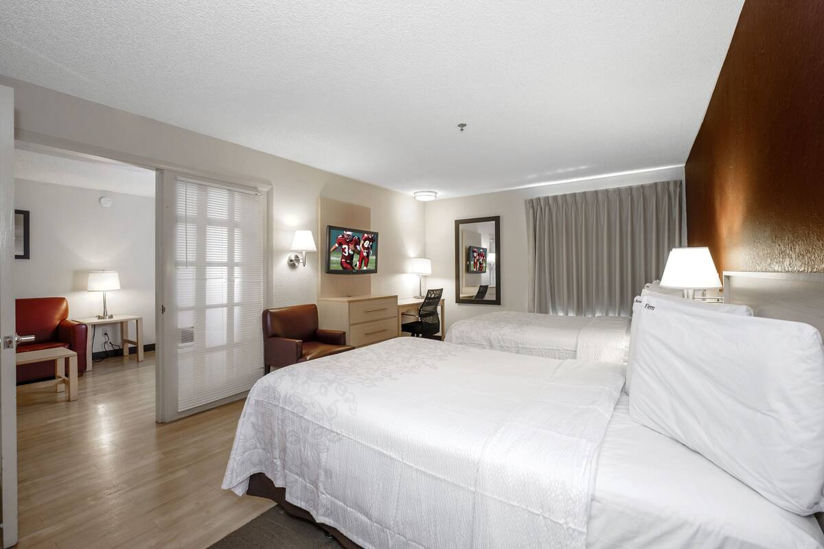 A hotel room with two beds, a desk, a chair, a lamp, and a large mirror.