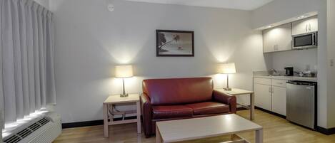 A compact living space with a sofa, a coffee table, a kitchenette, and a painting on the wall.