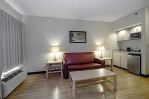 A compact living space with a sofa, a coffee table, a kitchenette, and a painting on the wall. - Red Roof Inn PLUS+ Gainesville (Gainesville)