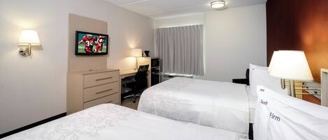 A hotel room with two beds, a desk, a chair, a television, and a window with curtains.