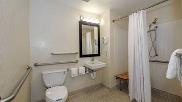 Un baño de hotel estándar con inodoro, lavamanos, espejo y ducha.