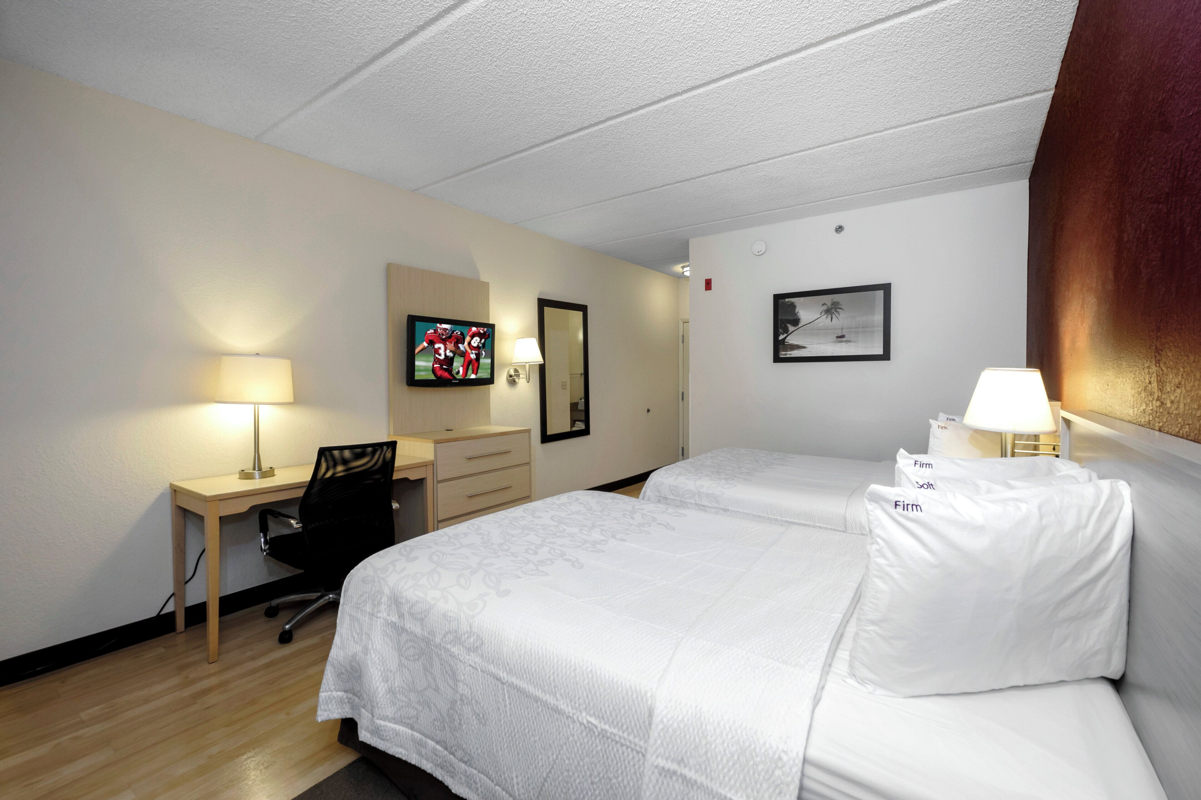 Habitación de hotel con dos camas, un escritorio, una silla, un televisor y un cuadro en la pared.