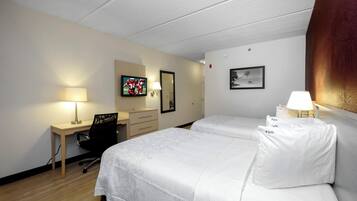 A hotel room with two beds, a desk, a chair, a TV, and a framed picture on the wall.