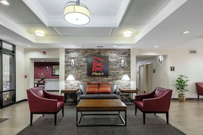 A lobby with a reception desk, a stone wall with a sign, a coffee table, two armchairs, and a potted plant.