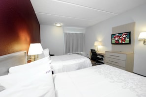 A hotel room with two beds, a desk, a chair, a television, and a lamp.