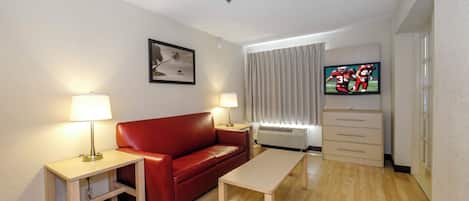 A hotel room with a red sofa, a wooden table, a TV, and a picture on the wall.