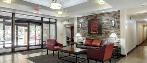 A hotel lobby with a reception desk, seating area, and a wall with a 'Red Roof Plus' sign.