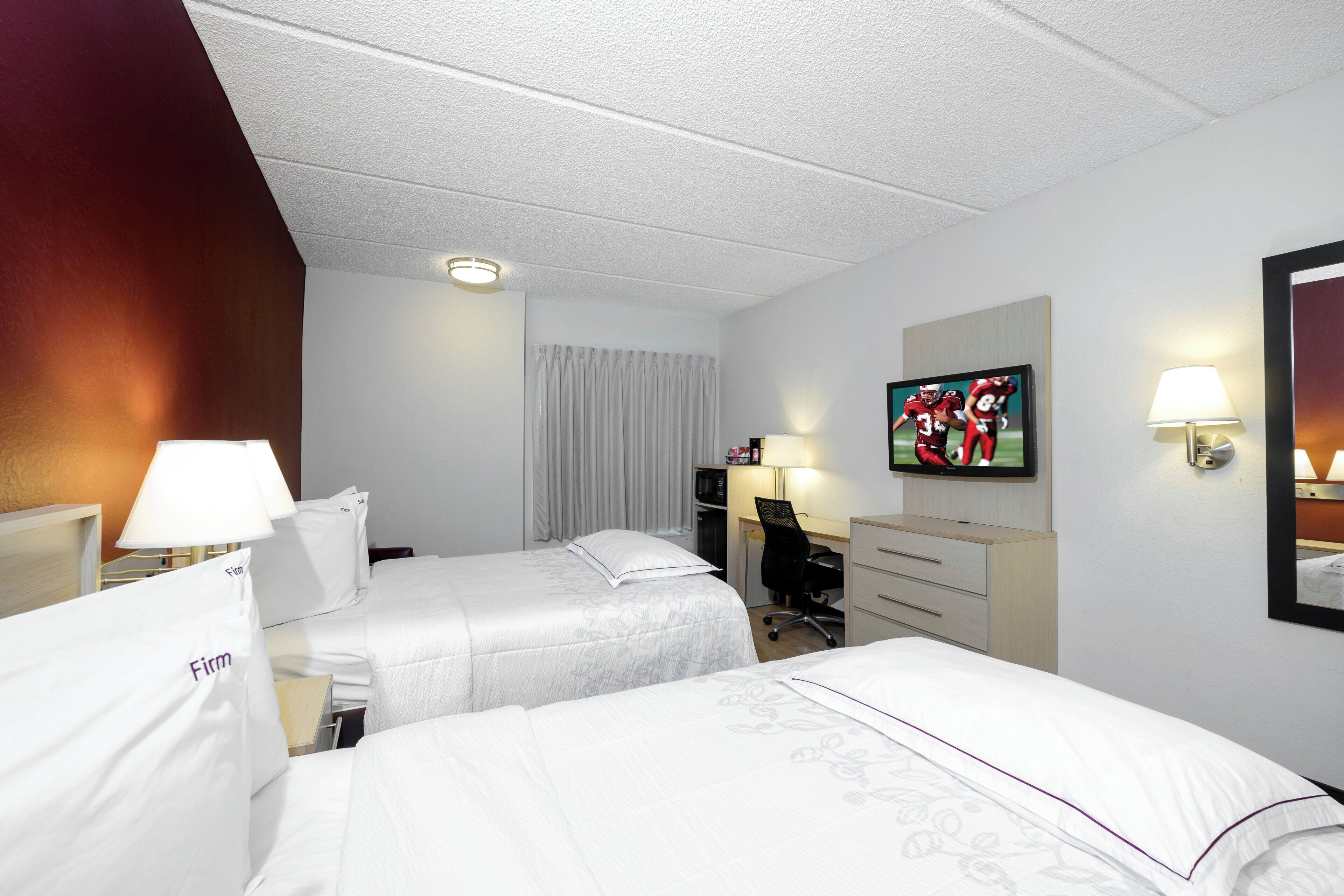 A hotel room with two beds, a desk, a chair, a television, and a mirror.
