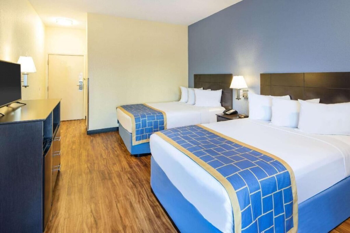 A hotel room with two beds, a desk, a television, and a door.