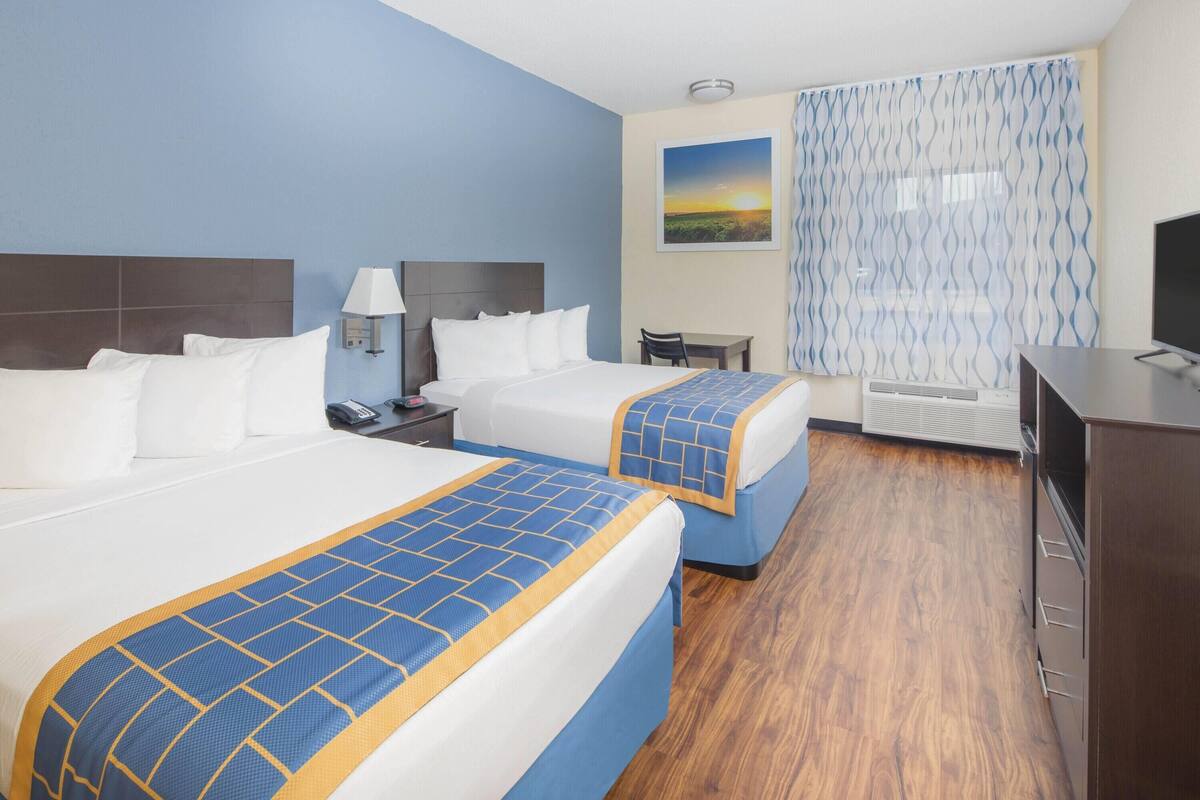 A hotel room with two beds, a desk, a chair, a TV, and a painting on the wall.