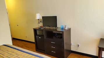 A hotel room with a bed, a desk with a computer, a lamp, and a TV.