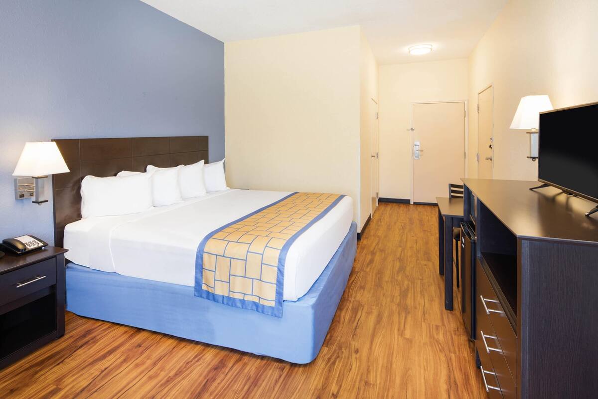 A hotel room with a bed, bedside lamps, a desk, and a television.