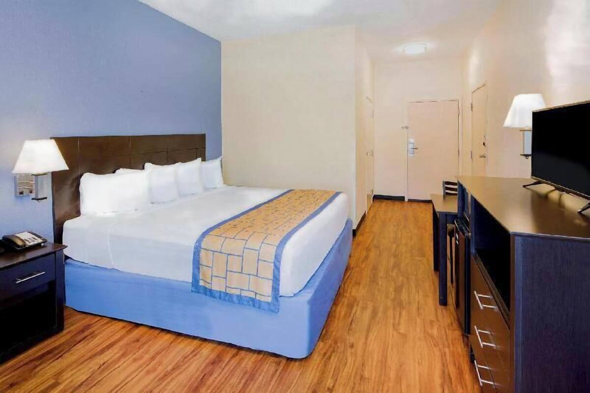 A hotel room with a bed, bedside tables, a desk, a television, and a door.