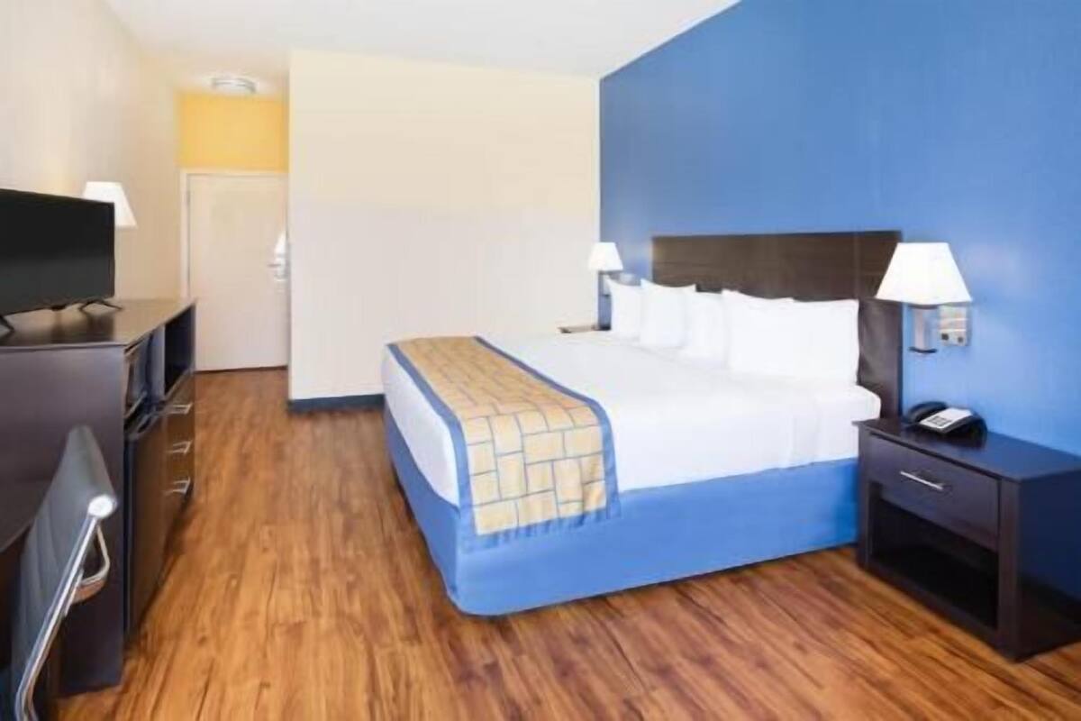 A hotel room with a bed, bedside tables, a TV, and a wooden floor.