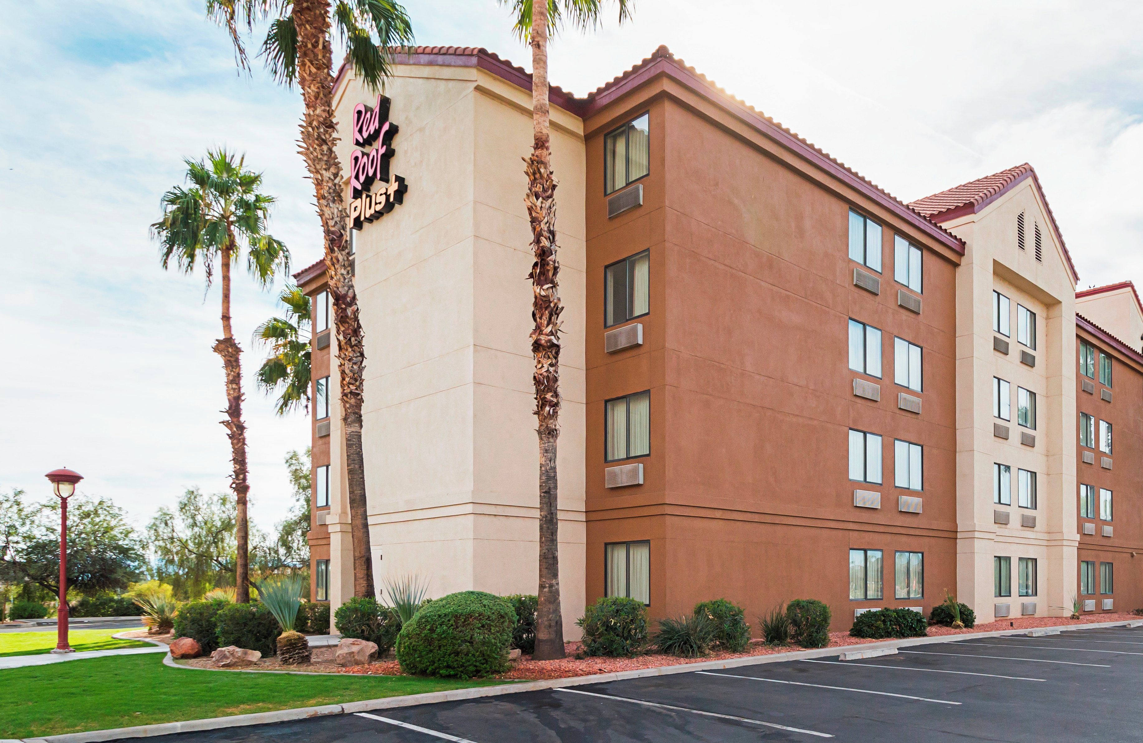 A multi-story hotel with a beige facade, palm trees, and a parking lot.