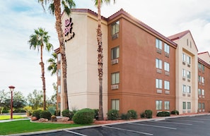 A multi-story hotel with a beige facade, palm trees, and a parking lot.